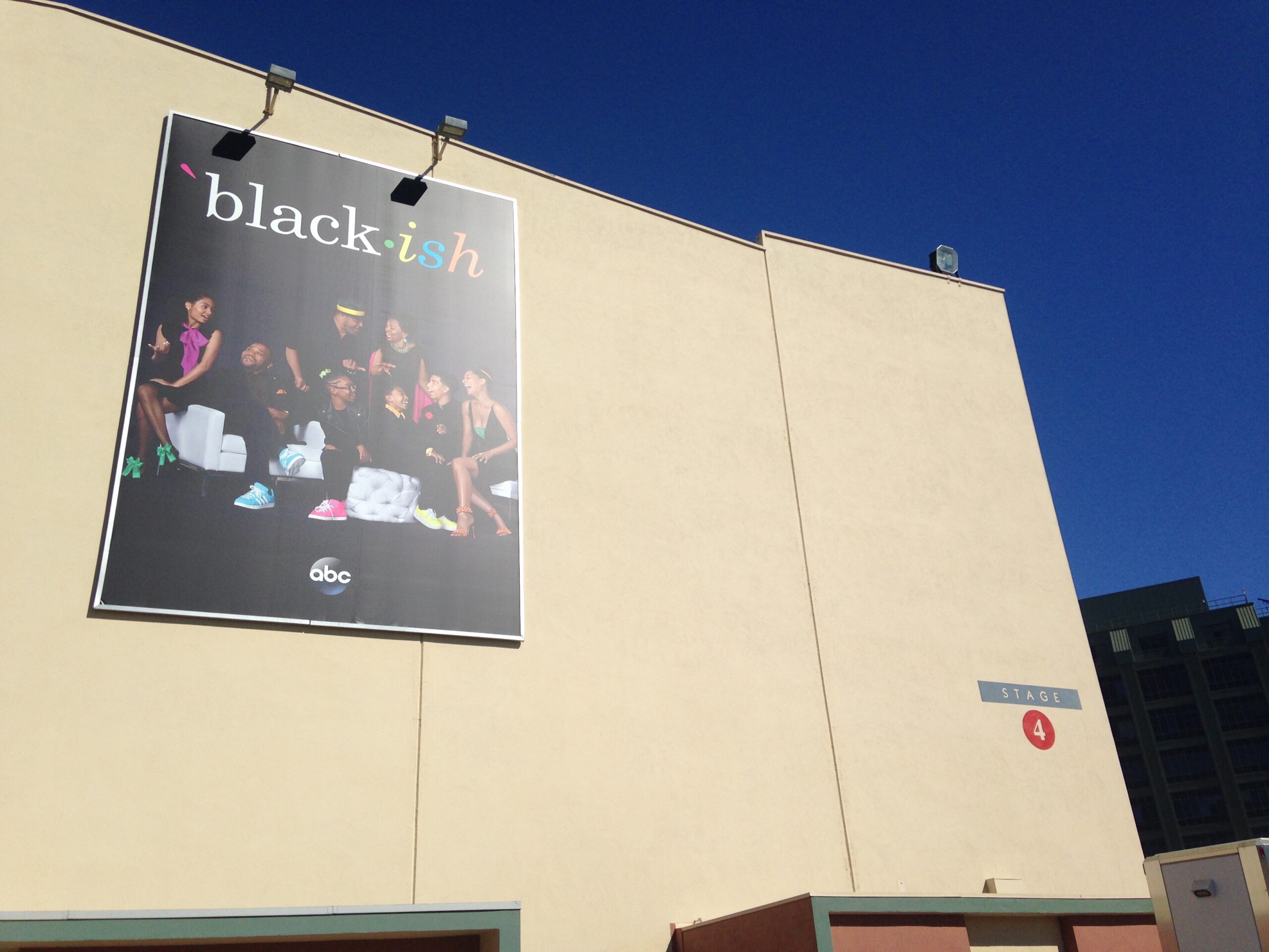 A large banner of the ABC TV show "Black-ish" is displayed on the exterior of a building marked as "Stage 4." The poster features the cast, suggesting a promotional or filming location related to the show.